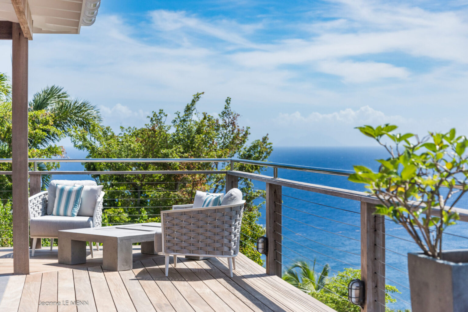 Wooden deck with grey lounge chairs overlooking the ocean.