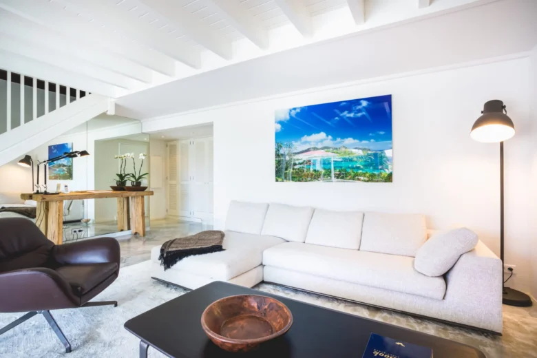 Modern white living room with a sectional sofa, leather armchair, and staircase.